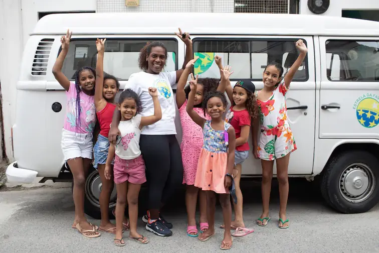 Een foto van kinderen van Estrela da Favela samen met een medewerker juichend voor een busje